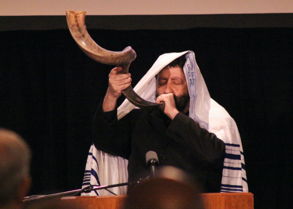 Rabbi Jonathan Cahn wearing a prayer shawl while blowing a shofar 
